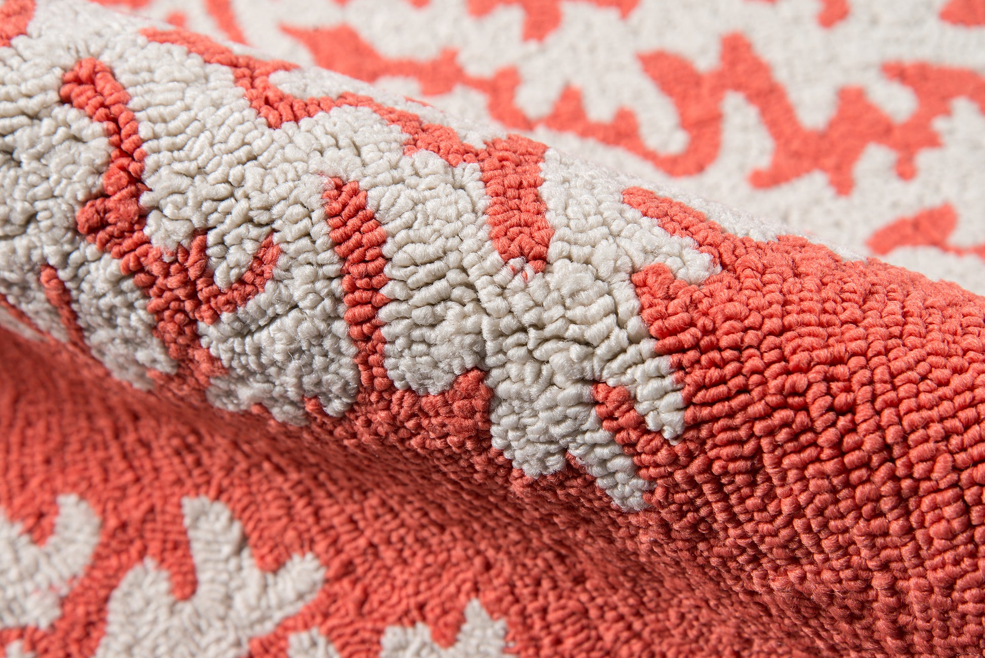 Close-up of coral and ivory loop-pile rug with thick textured fibers; rolled edge, cozy home decor.