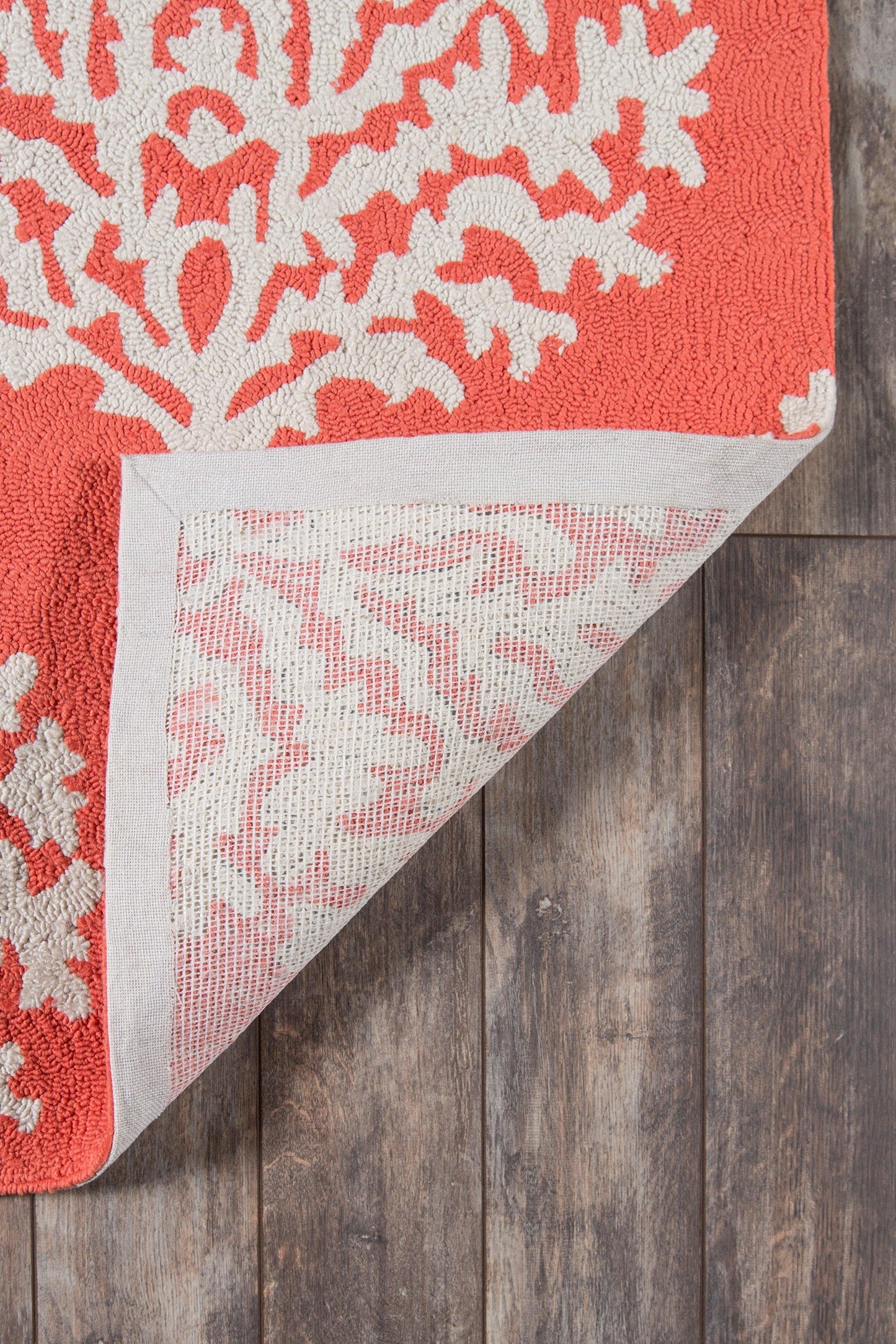 Orange rug with white botanical motif; woven textile, folded corner reveals reverse weave on wood floor.