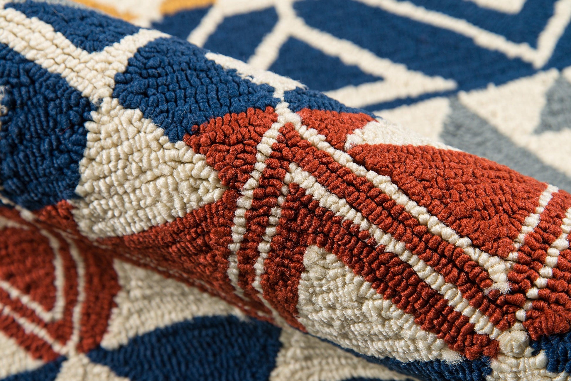Close-up of a tufted geometric rug in navy, red and cream with bold triangular shapes.