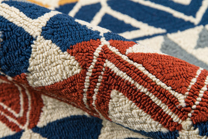 Close-up of a tufted geometric rug in navy, red and cream with bold triangular shapes.
