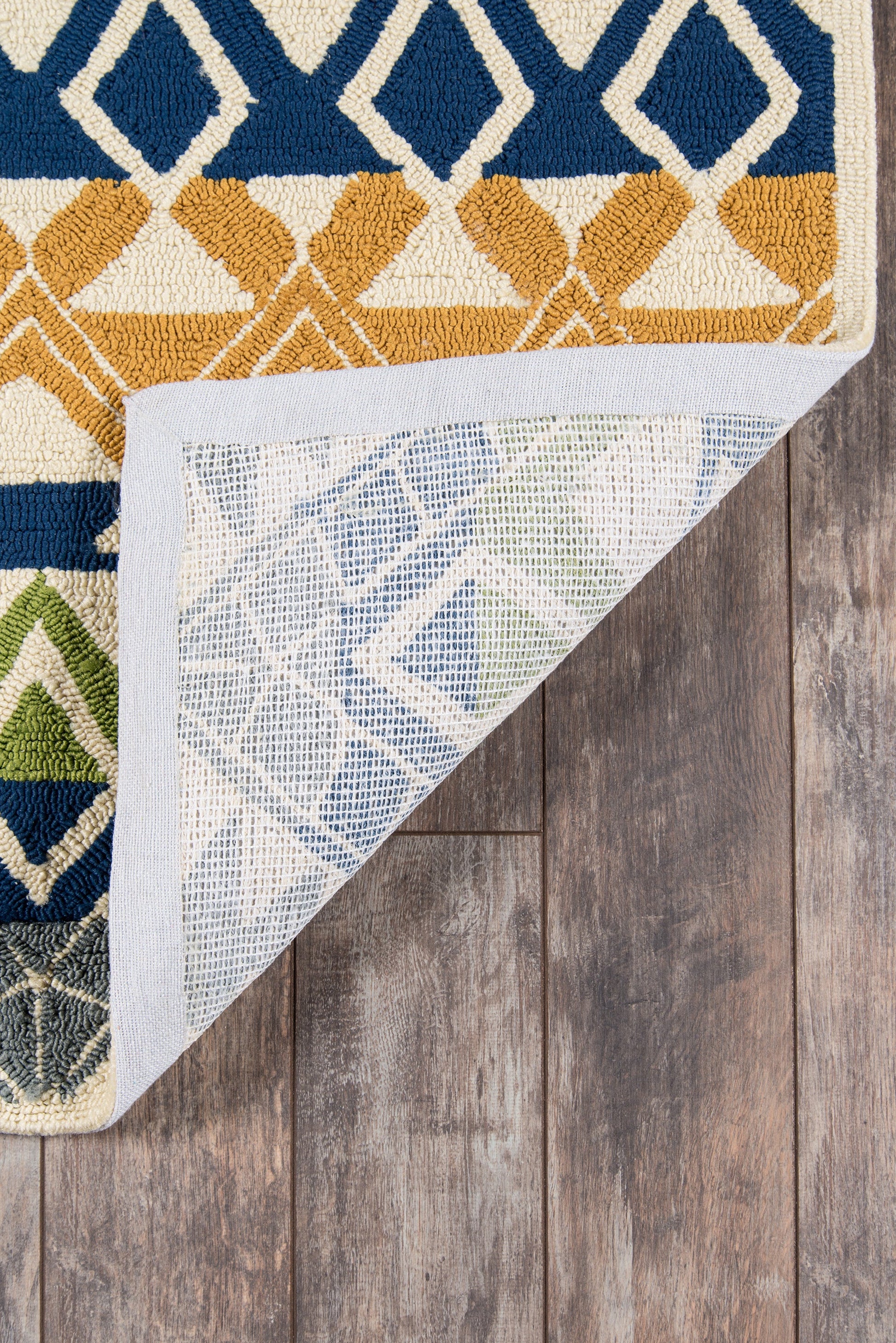Geometric tufted area rug in navy, mustard and cream with diamond shapes; folded corner reveals woven underside on wood floor.