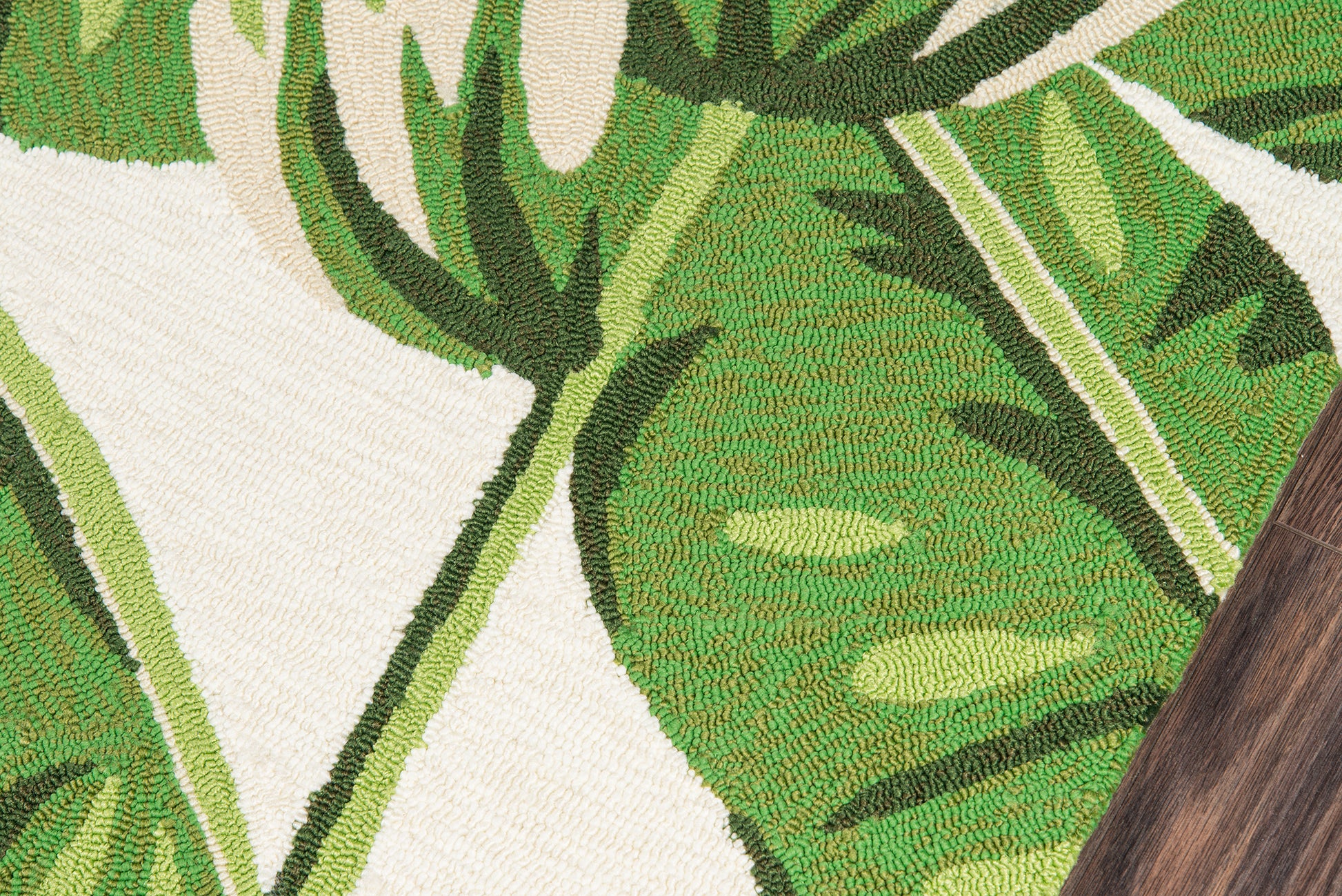Close-up of a woven rug with tropical green leaves on a cream background and a wood floor edge.