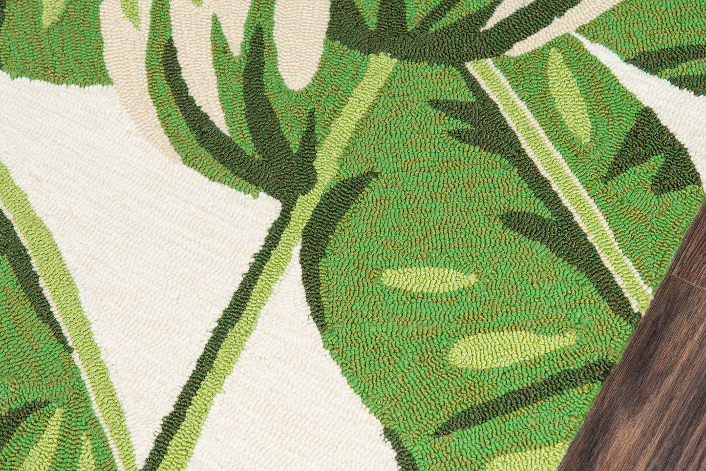 Green monstera leaf rug with bold botanical pattern on light ivory background; woven texture, rustic style.