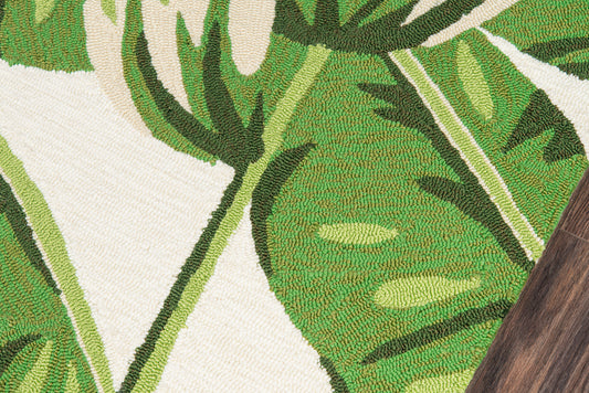 Green monstera leaf rug with bold botanical pattern on light ivory background; woven texture, rustic style.
