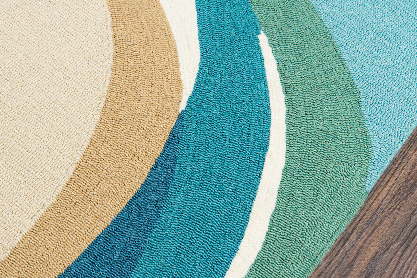 Woven round area rug with curved color bands in beige, tan, teal, blue and green on wood floor.