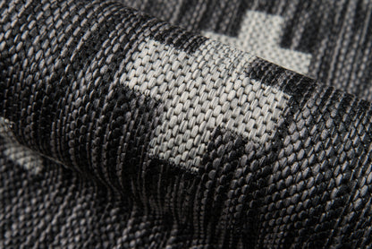 Close-up of dark gray and black woven fabric with light gray geometric blocks; rugged textile for upholstery or rugs.