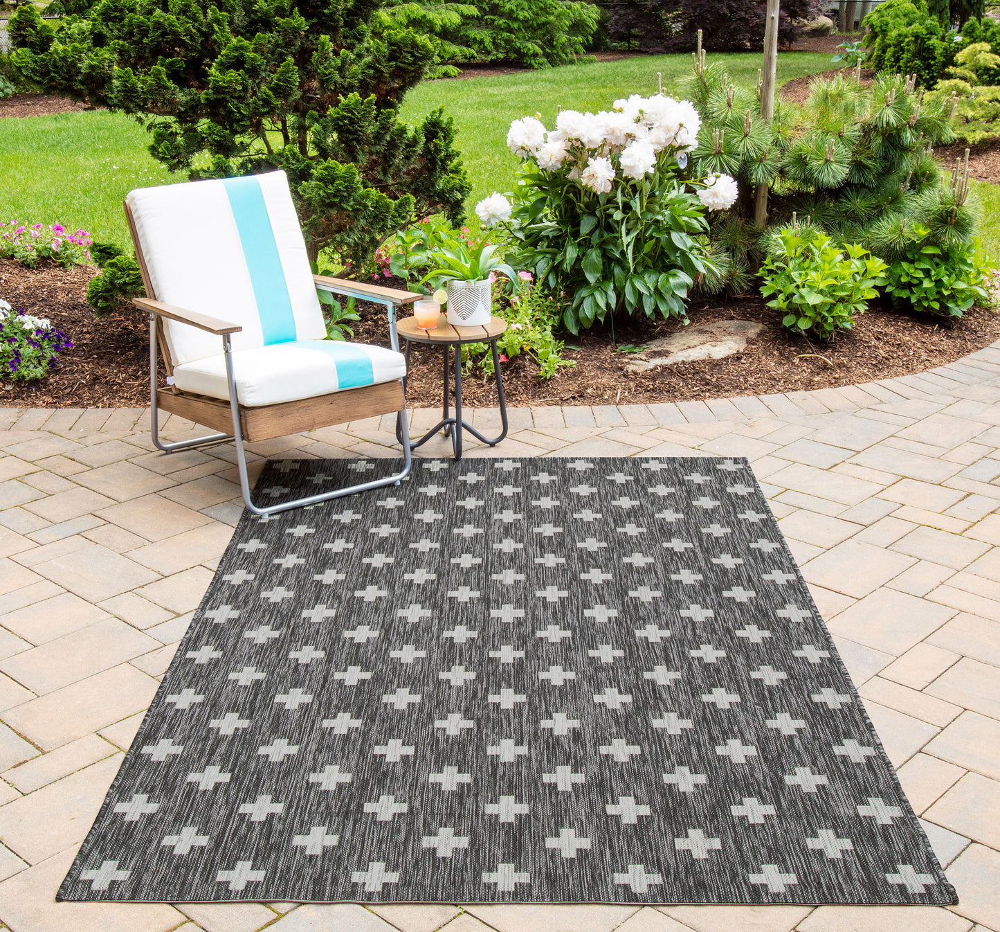 Outdoor patio with cushioned wooden chair, blue striped cushion, side table with plants, and a gray cross-pattern rug.