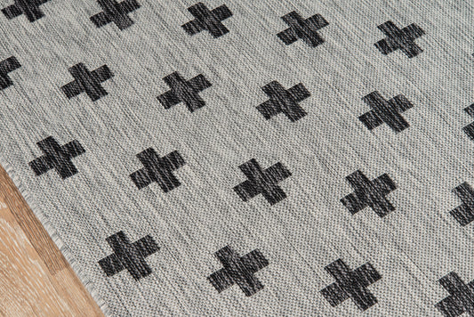 Grey woven rug with repeating black cross motif; soft textured fabric on wooden floor.