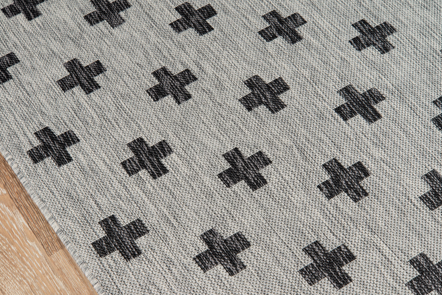 Gray woven rug with repeating black plus-cross motifs on a light gray background.