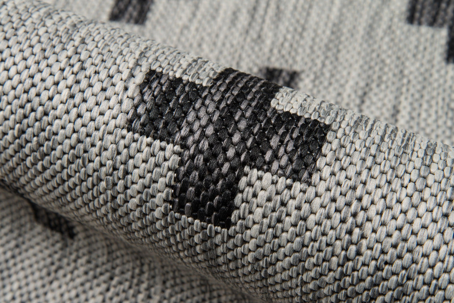 Gray woven rug with black geometric squares, close-up of textured fabric.