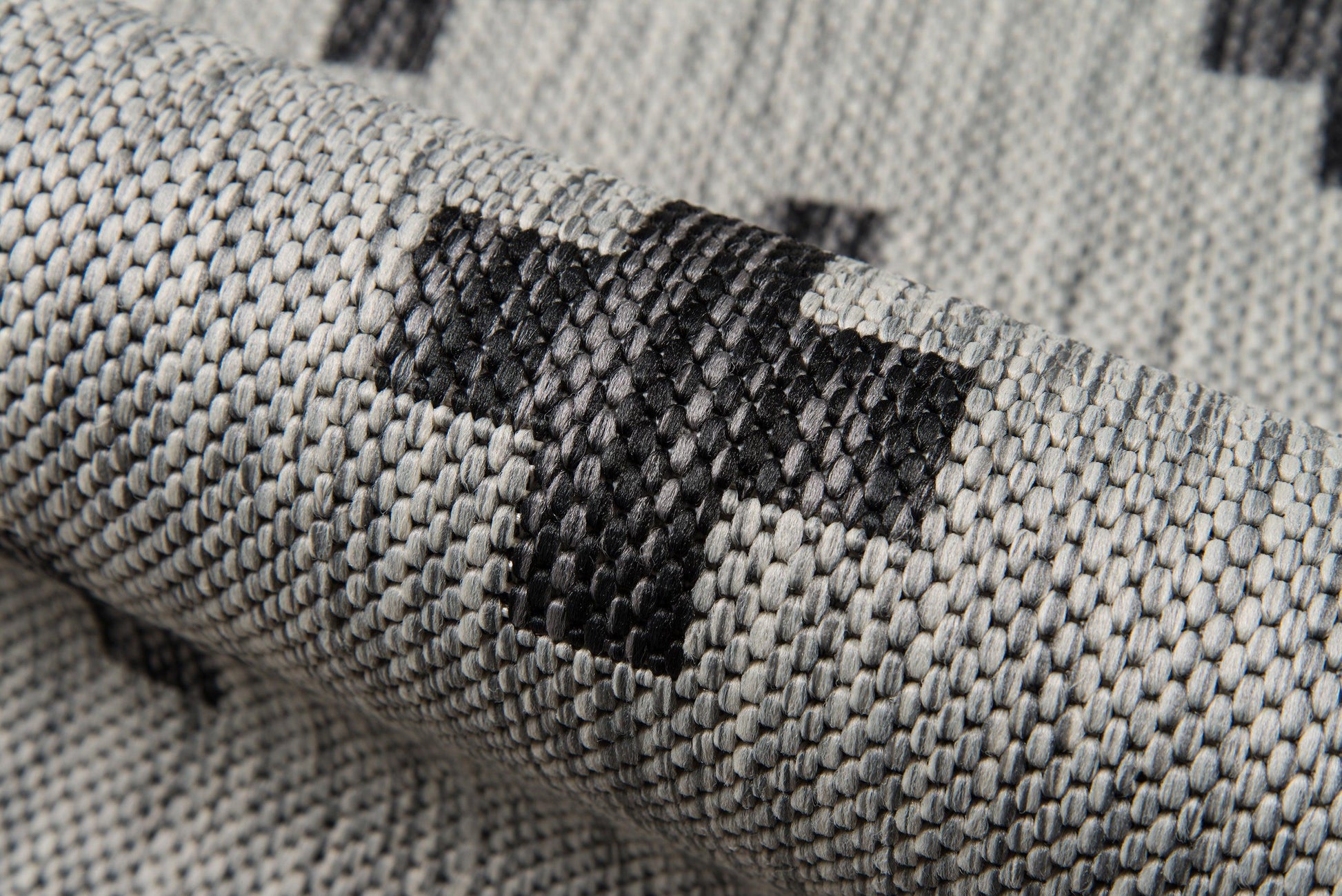Gray woven rug with black geometric squares, close-up of textured fabric.