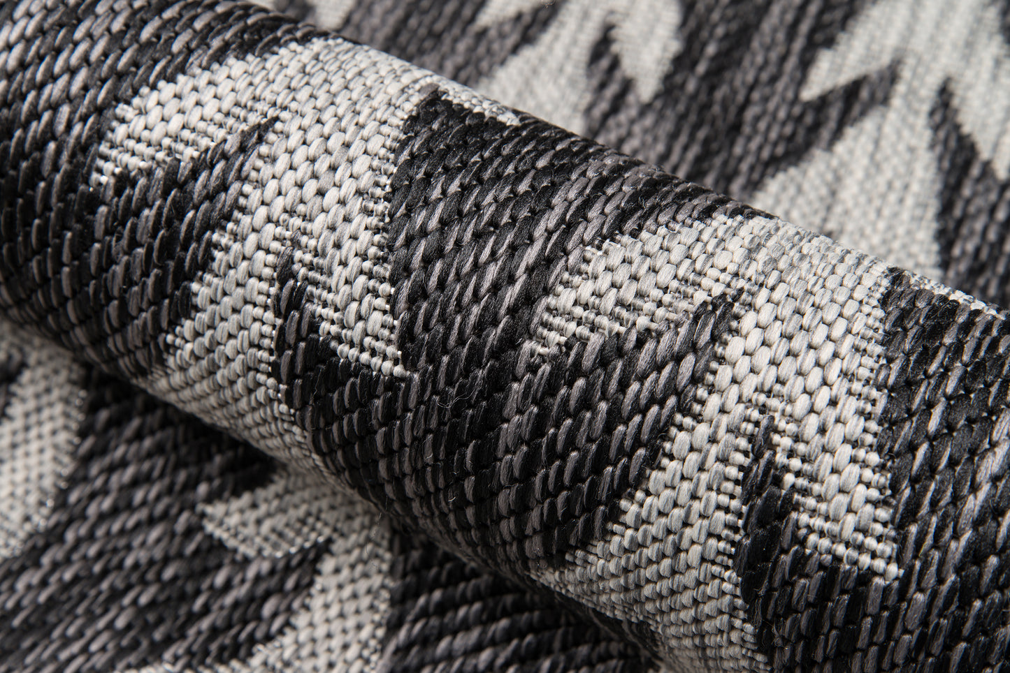 Rolled black-and-gray woven rug with a bold geometric leaf-like pattern; textured rug.