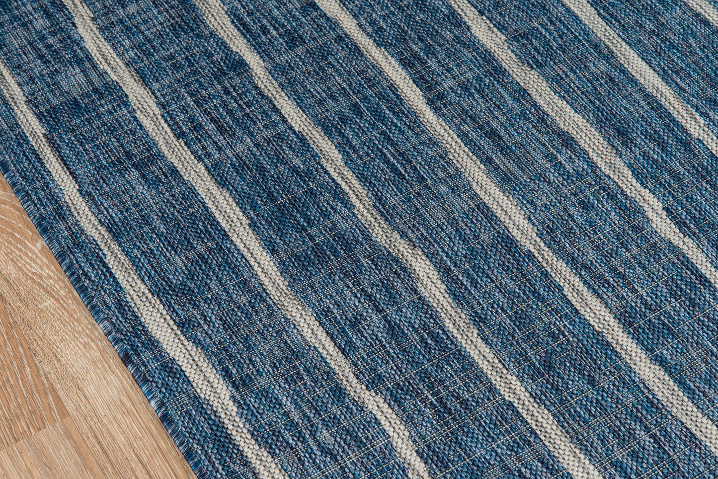 Blue striped woven area rug with cream stripes laid on wooden floor.