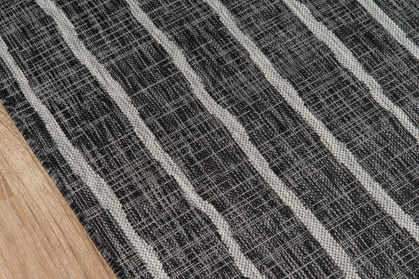 Dark charcoal woven rug with light gray diagonal stripes on a wood floor.