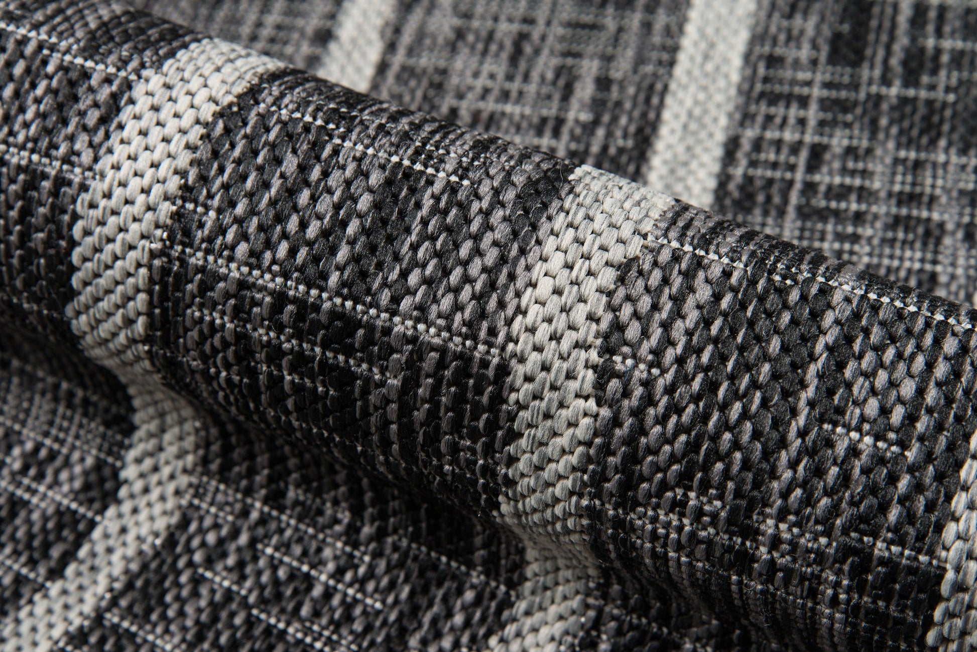 Macro close-up of a black, gray and ivory woven textile with chunky striped pattern and rolled edge.