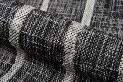 Close-up of black, gray and white woven rug fabric with chunky texture, striped pattern, folded roll.
