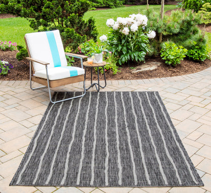 Outdoor patio chair with white cushion and turquoise stripe, metal frame; round side table and striped gray rug in garden.