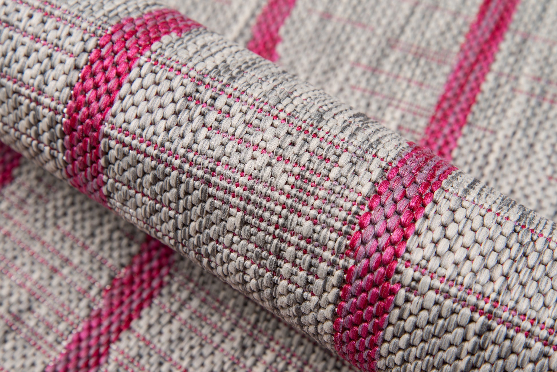Close-up of a beige woven rug with bright pink stripes, textured fibers, rolled corner.