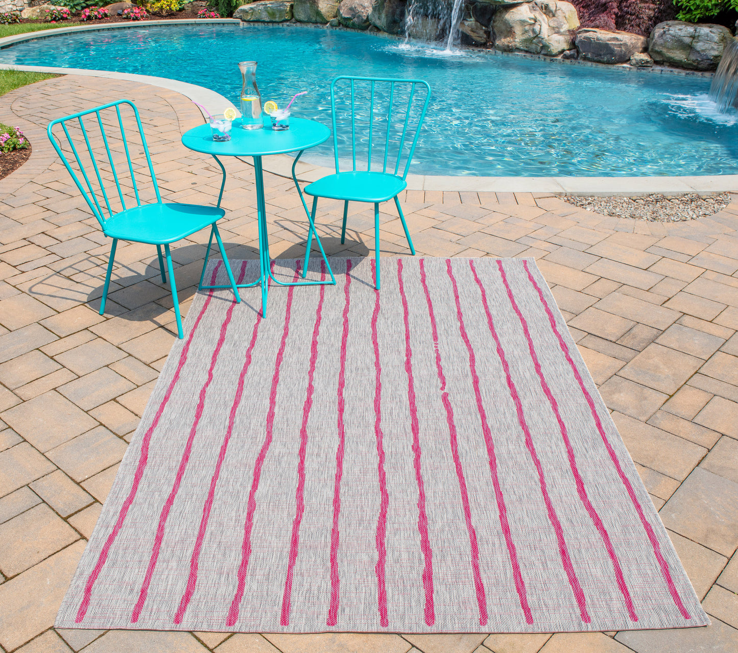 Rectangular outdoor rug with pink stripes on beige, brick patio, turquoise metal bistro chairs and table by the pool.
