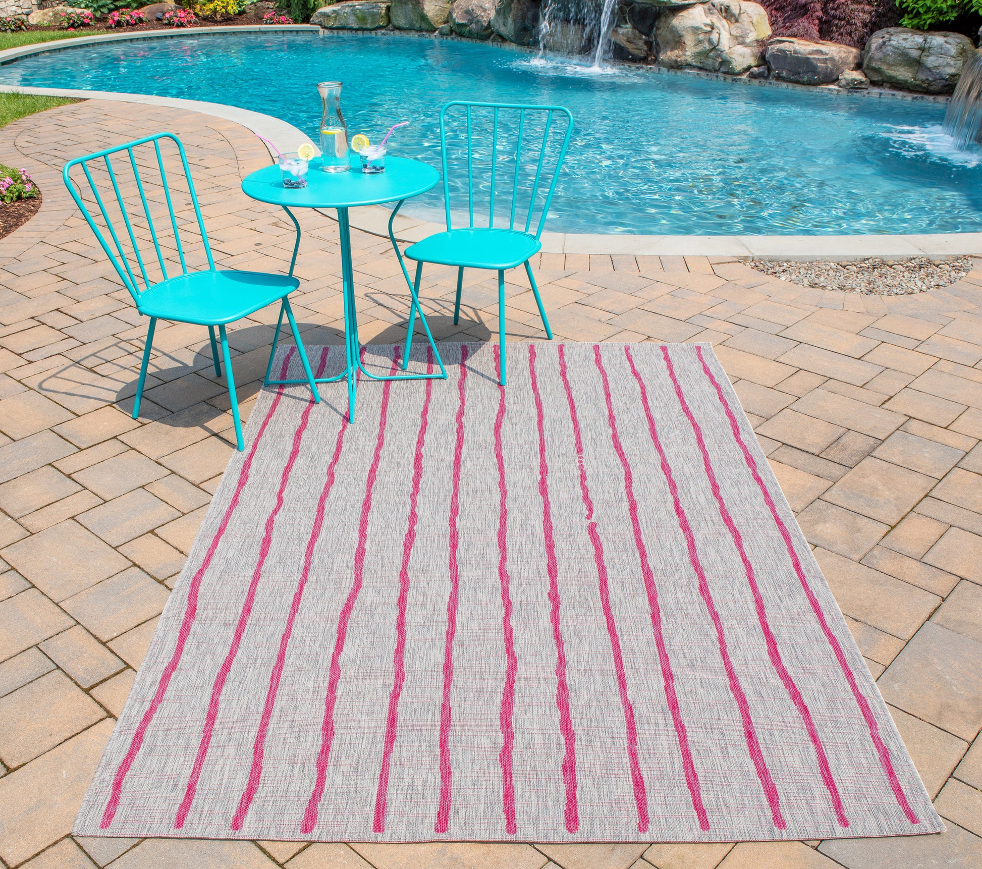 Rectangular outdoor rug with pink stripes on beige, brick patio, turquoise metal bistro chairs and table by the pool.
