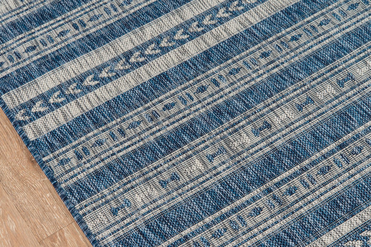 Blue woven area rug with beige geometric stripes on a wooden floor.