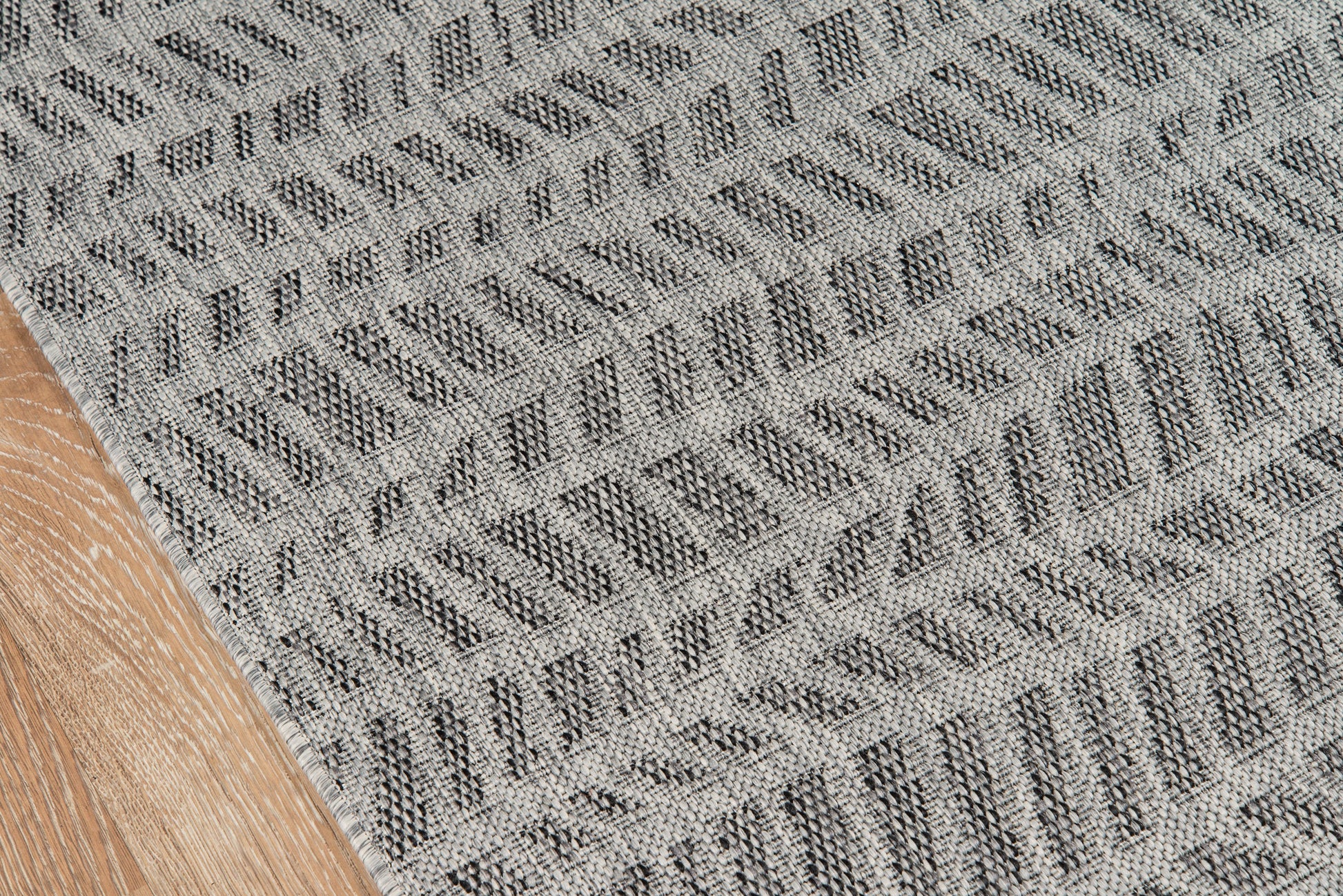 Gray textured woven rug with diagonal chevron pattern, laid on a wooden floor.