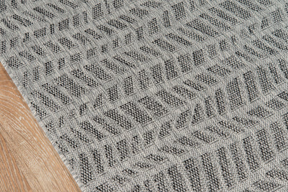 Gray textured woven rug with diagonal chevron pattern, laid on a wooden floor.