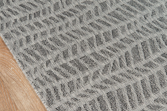 Gray textured rug with repeating chevron geometric pattern on a wooden floor.