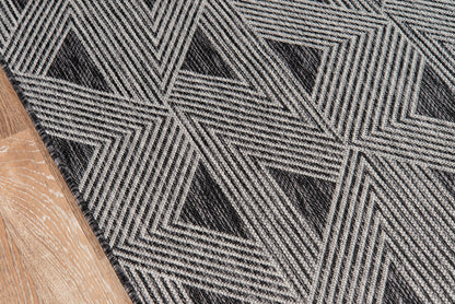 Geometric gray and black rug with interlocking triangular chevron pattern; wood floor edge visible.