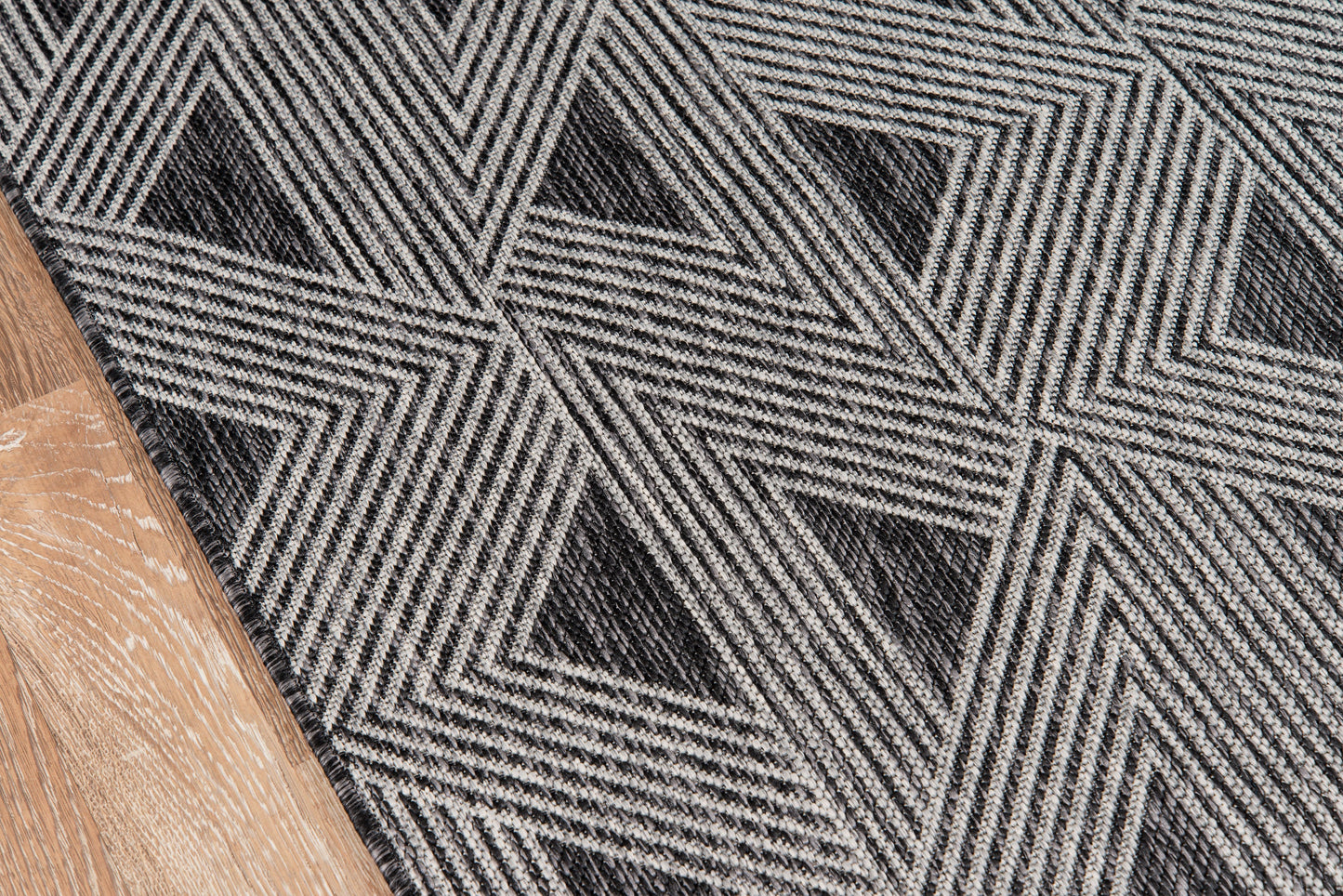 Chevron geometric rug in black and gray, woven textured pattern on wood floor, modern entryway style.