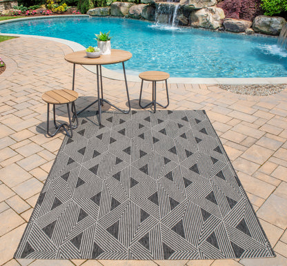 Outdoor poolside patio with geometric gray rug, round wood-top table & two matching stools.