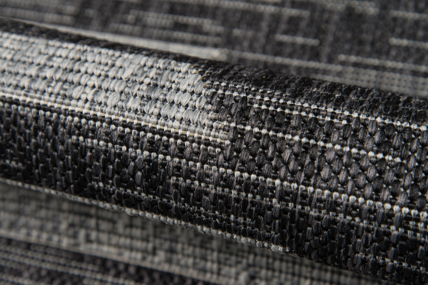 Close-up of charcoal gray woven rug with textured tweed weave and subtle geometric border.