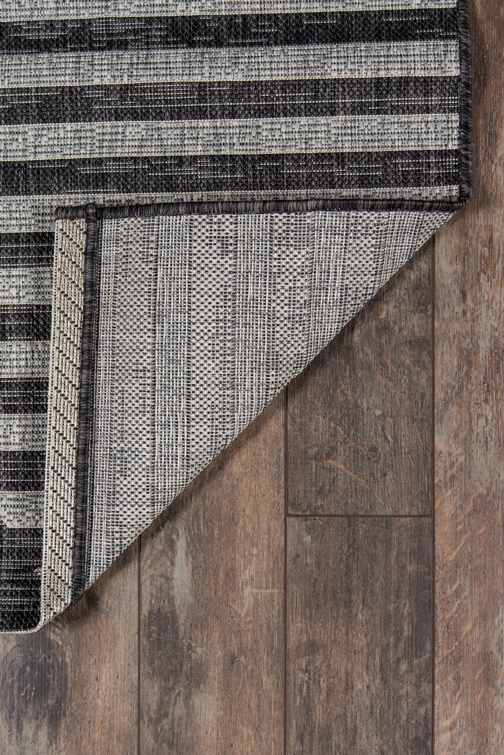 Two-tone striped woven rug with folded corner on dark wooden floor.