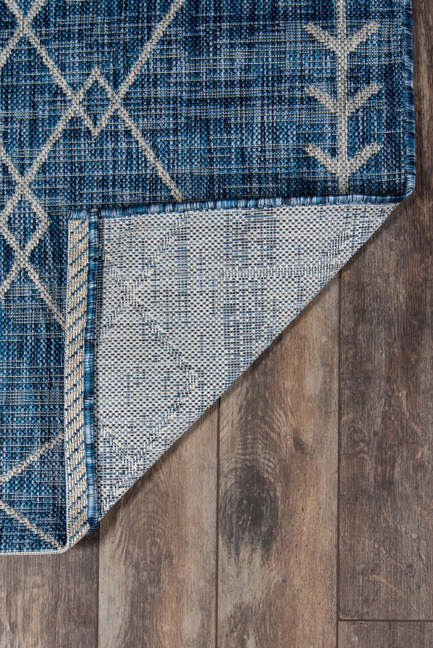 Blue geometric woven rug with white line pattern, folded corner reveals lighter underside on wooden floor