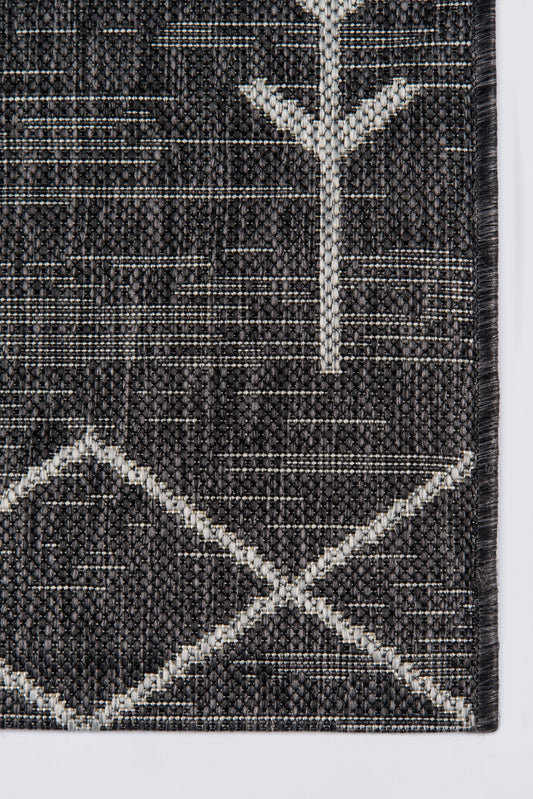 Charcoal woven rug with ivory geometric lines forming diamonds and a Y-shaped motif; textured pile.