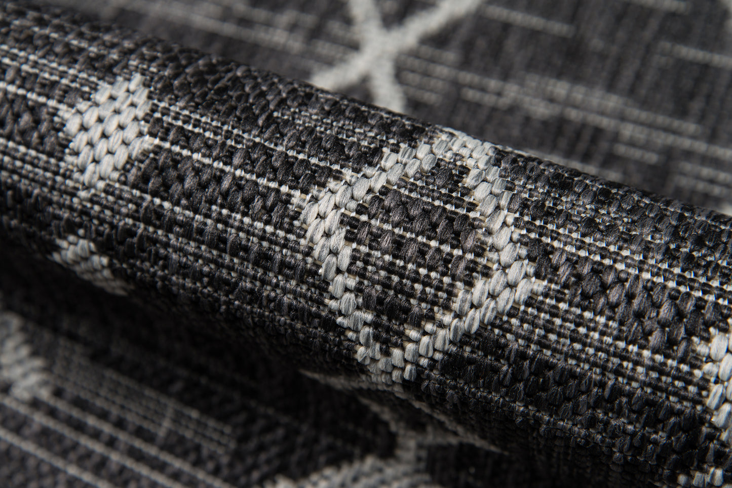 Close-up of a dark gray woven rug with a light gray geometric diamond pattern; textured surface.