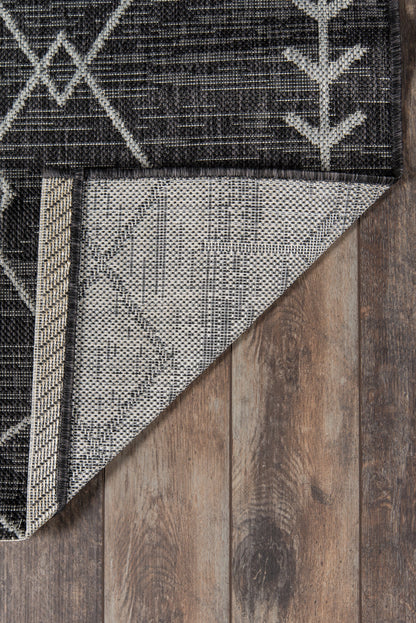 Dark charcoal geometric rug with white linear patterns, folded corner reveals lighter underside on wooden floor.