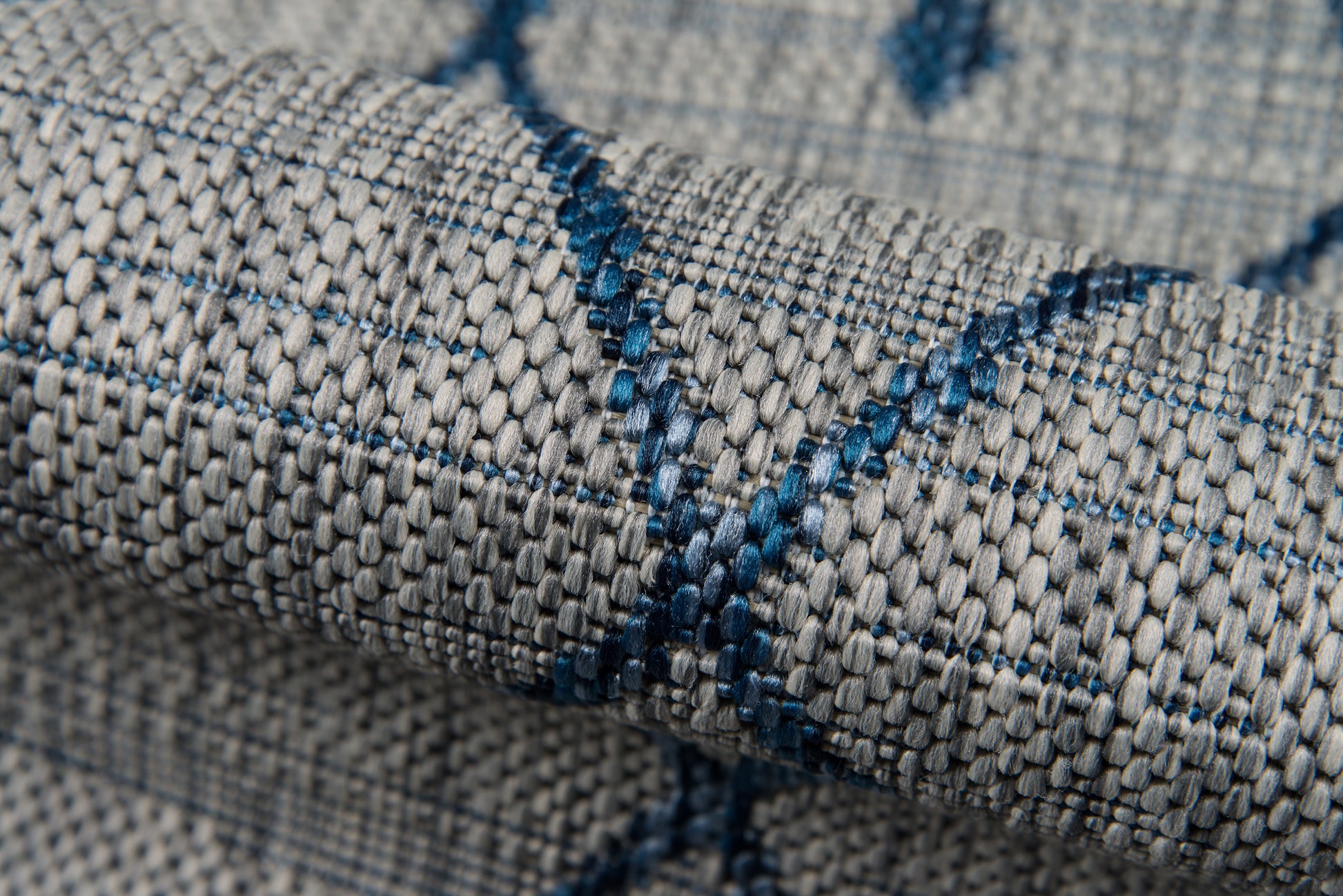 Close-up of a gray woven rug with blue thread lines forming a subtle geometric pattern.