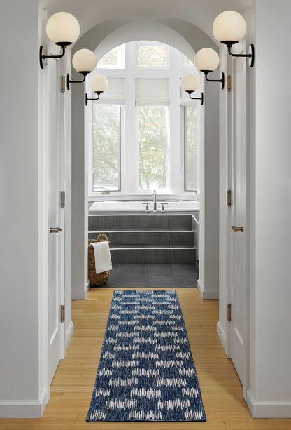 Blue geometric patterned runner rug down a white hallway with arched doorway and globe wall sconces.