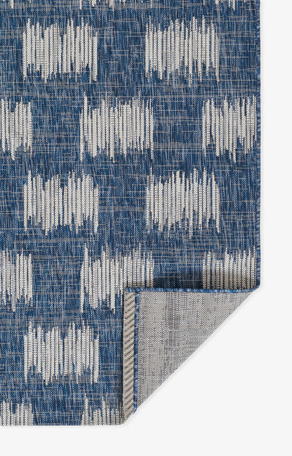 Blue woven rug with white geometric blocks; rectangular, modern living-room accent with folded gray backing.