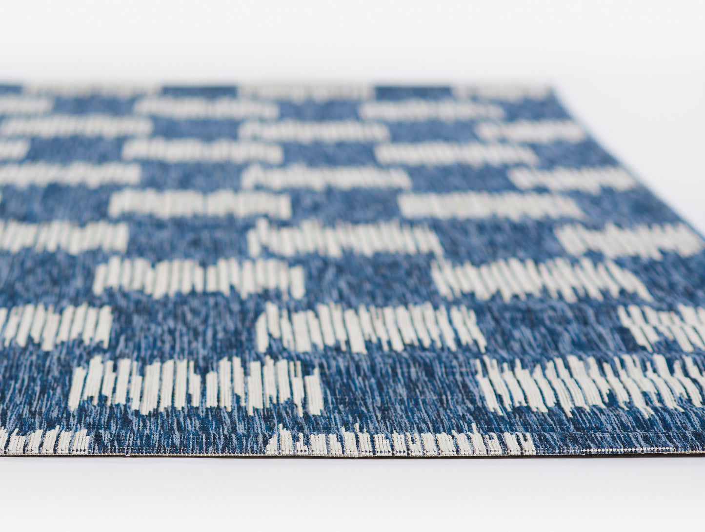 Rectangular blue woven rug with white geometric stripe pattern; modern flat-weave style for living room decor.