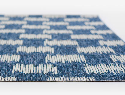 Rectangular blue woven rug with white geometric stripe pattern; modern flat-weave style for living room decor.