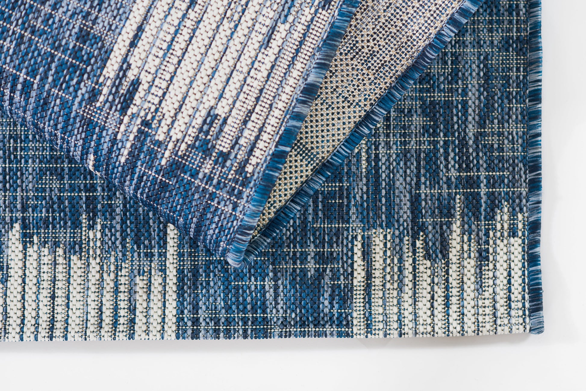 Blue woven runner rug with white and dark blue linear pattern, folded to show fringe and underside.
