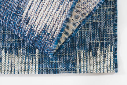 Blue woven runner rug with white and dark blue linear pattern, folded to show fringe and underside.