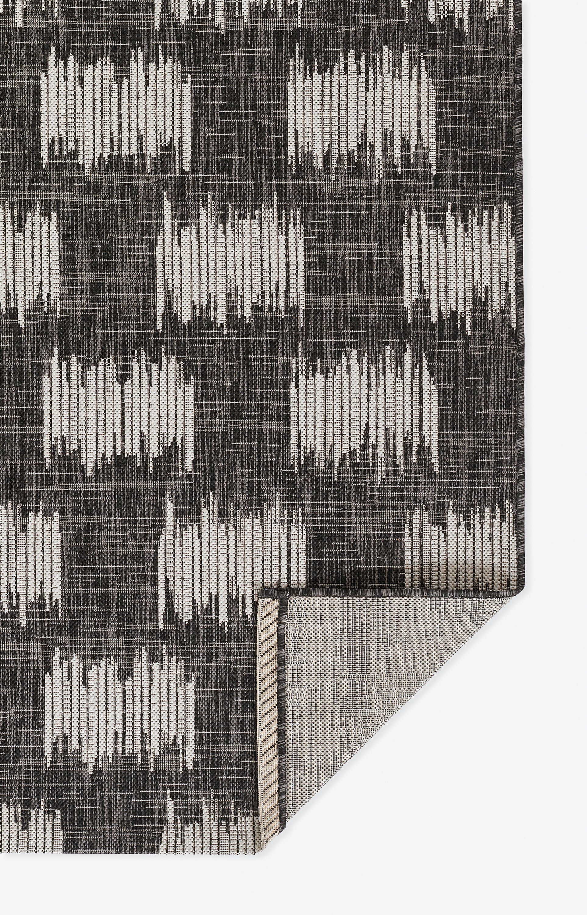 Charcoal and ivory geometric woven rug with rectangular block motifs; folded corner reveals beige backing.