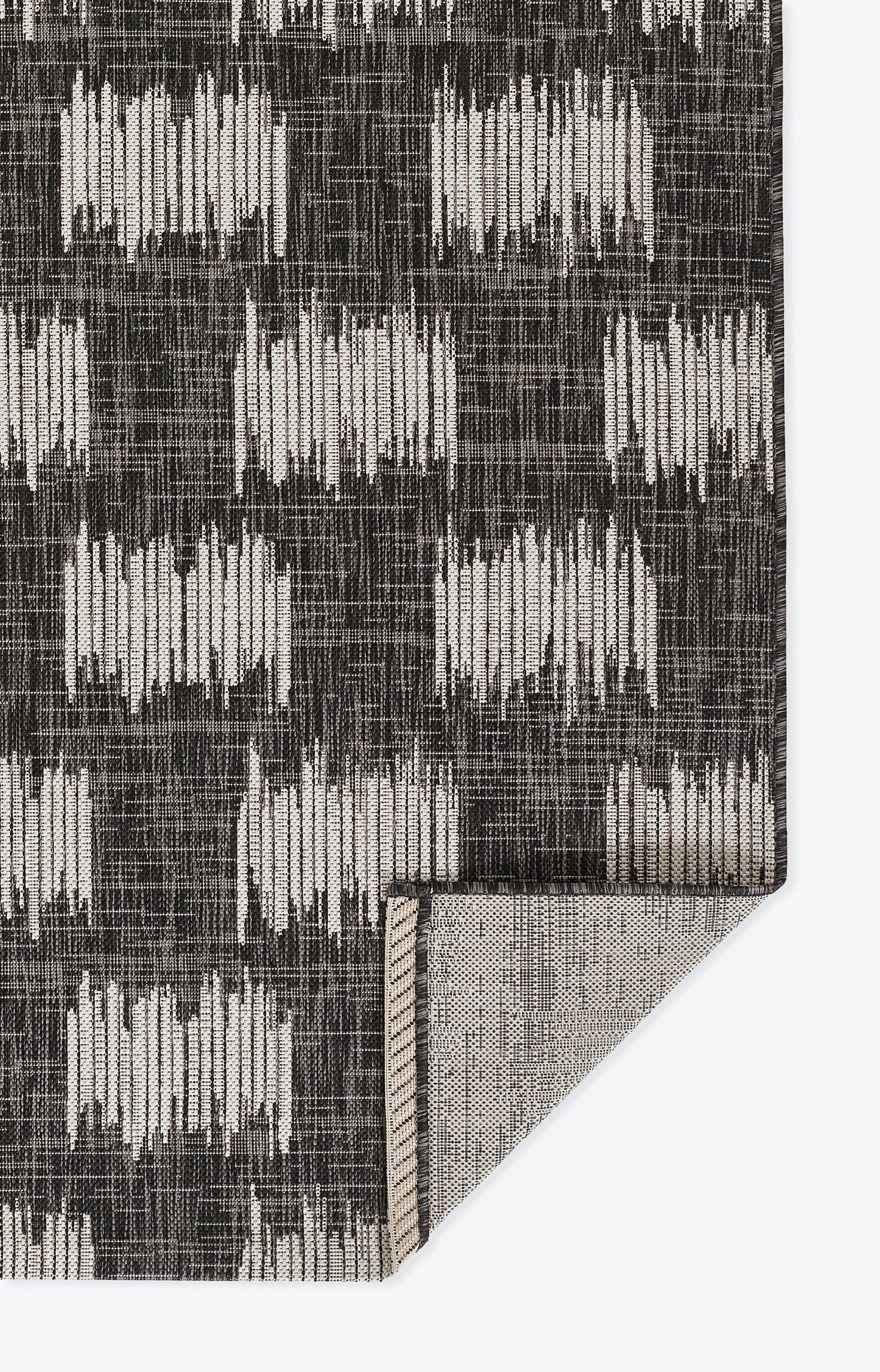 Charcoal rug with cream rectangular ikat-like blocks, woven texture, folded corner showing light underside.