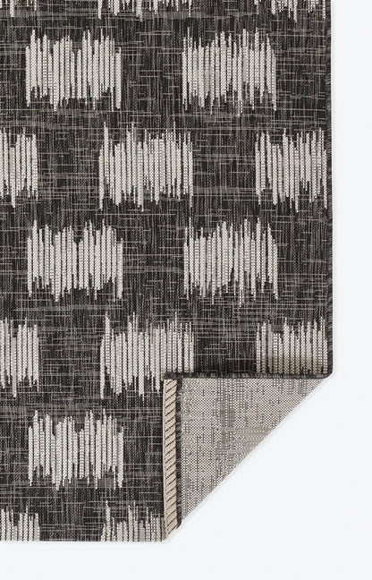 Charcoal runner with ivory vertical brushstroke blocks in a grid; woven texture, folded corner shows beige backing.