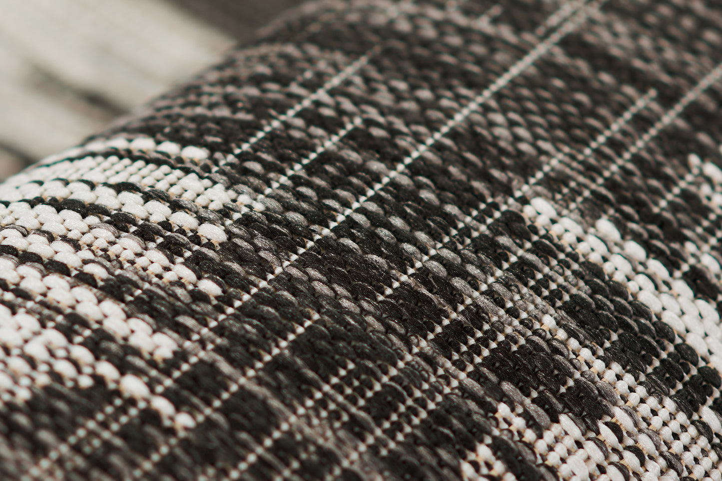 Close-up of black and white tweed rug with a plaid grid weave, showcasing a textured surface.