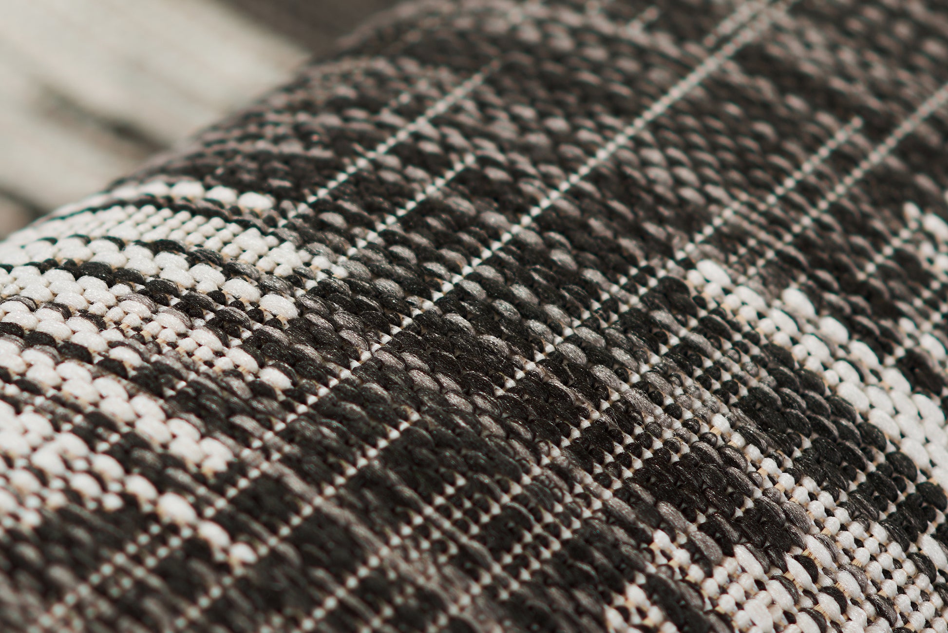 Close-up of black and white tweed rug with a plaid grid weave, showcasing a textured surface.