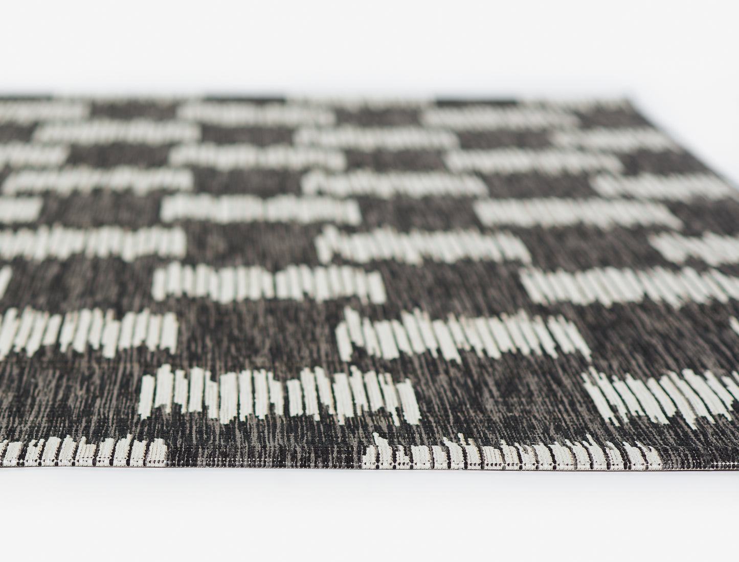 Charcoal and white geometric rug with checkerboard block pattern, flat-weave texture, bound edge.